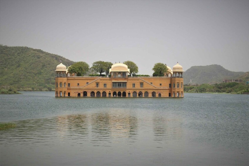 A large, multi-story building with domed roofs on an island in a body of water, surrounded by hills. 4