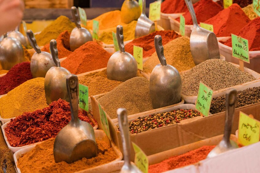A variety of spices displayed in containers with metal scoops and price tags. 2