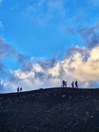 A group of people hiking on a rocky hill with a partly cloudy sky. 1