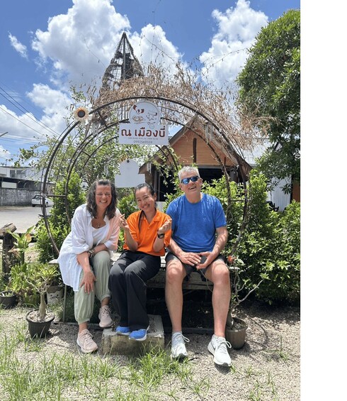 Three people sitting on a bench in front of a mosque with a signboard. 3
