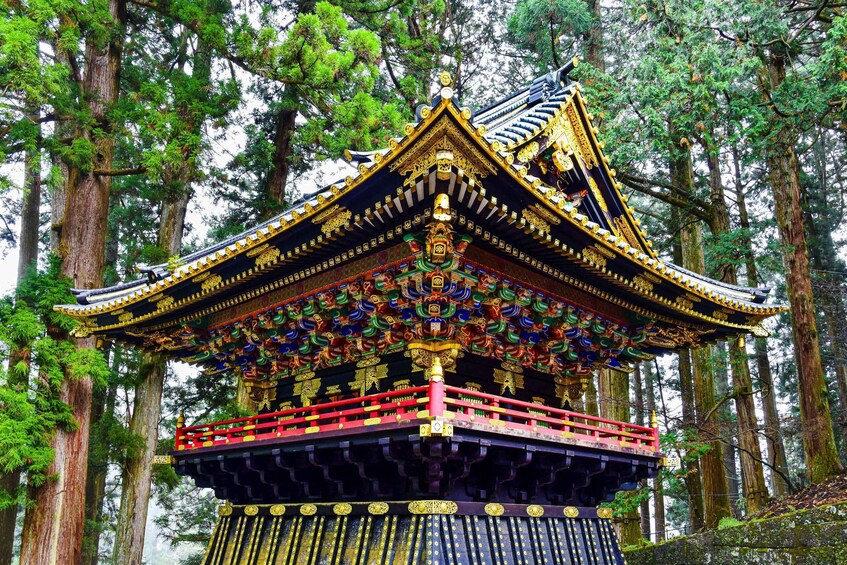 A traditional temple with ornate golden decorations and a red railing, surrounded by tall trees. 2