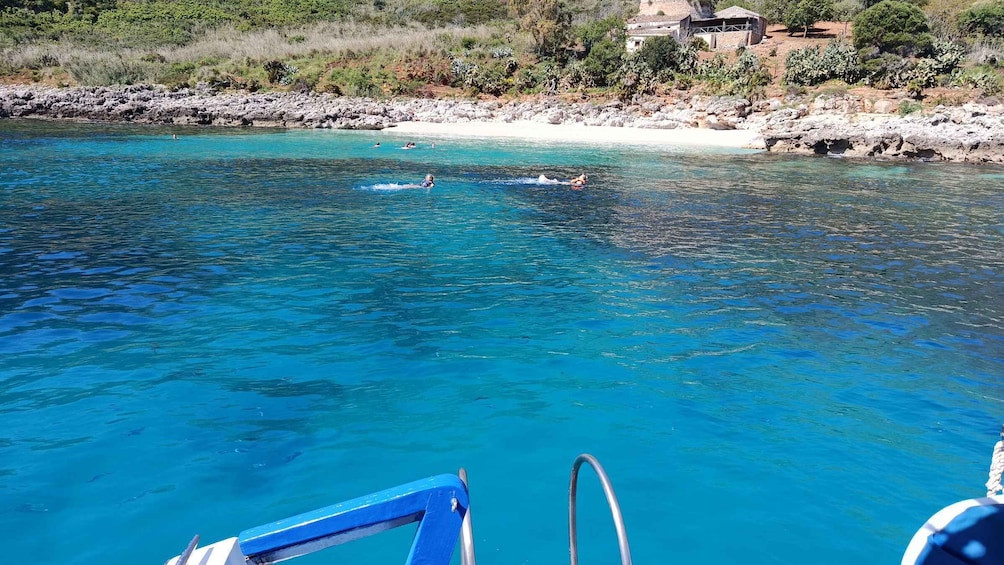 A clear blue sea with a rocky shoreline, a boat with a blue railing, and a building in the background. 4