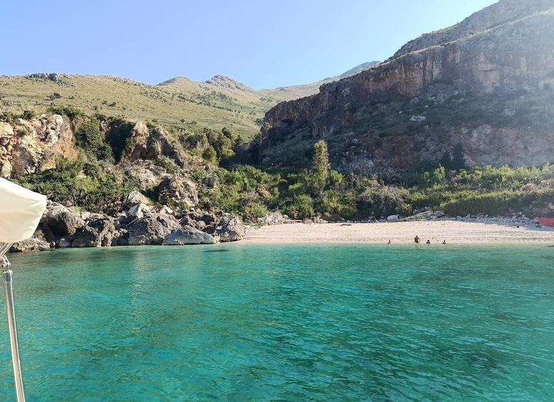 A coastal landscape with clear turquoise waters, rocky cliffs, and a sandy beach. 3