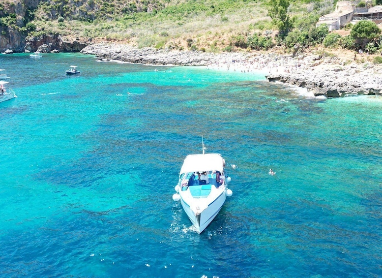A boat on clear turquoise waters with rocky coastline and sparse vegetation. 1