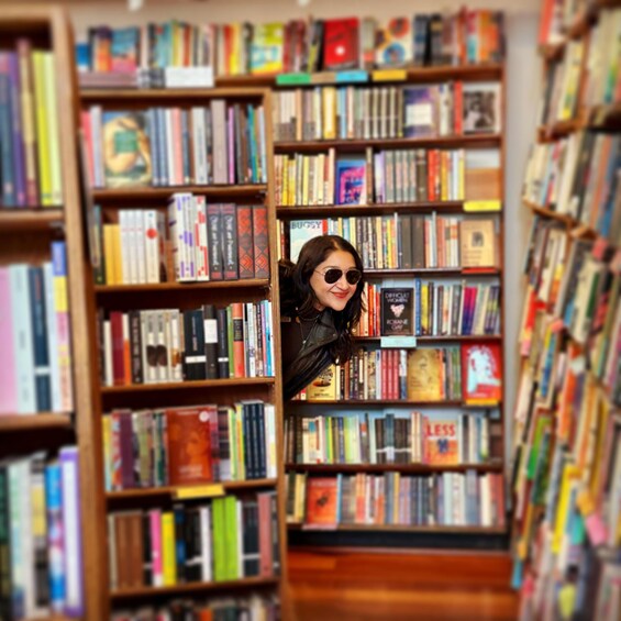 A person peeking through a gap in a bookshelf filled with books. 5