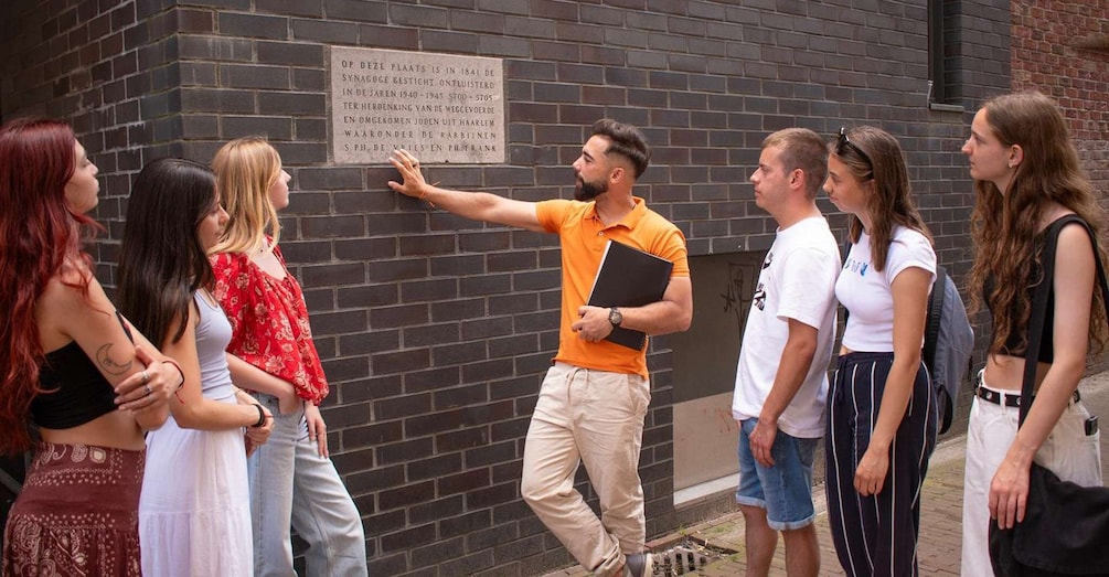 A group of people standing in front of a brick wall with a historical plaque. 4