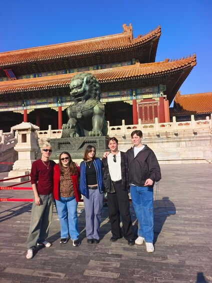 A group of people posing in front of a traditional Chinese building with ornate architecture and a bronze lion statue. 1