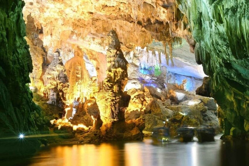 A cave with illuminated stalactites and stalagmites, a reflective pool, and green cave walls. 3