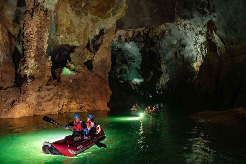 A group kayaking in a cave with illuminated water and rocky walls. 4