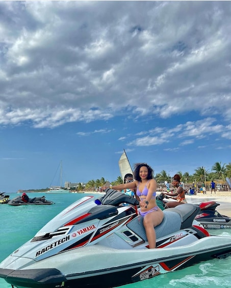 Une personne sur un jet ski Yamaha, sur une plage bordée de palmiers, avec un voilier en arrière-plan. 4