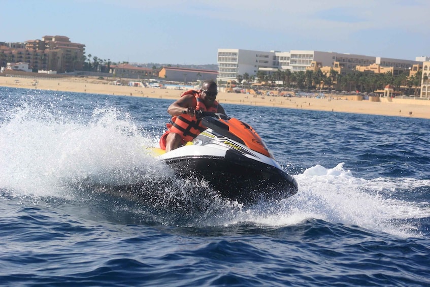 Une personne pratiquant le jet-ski sur une étendue d’eau, avec une plage et des bâtiments en arrière-plan. 3