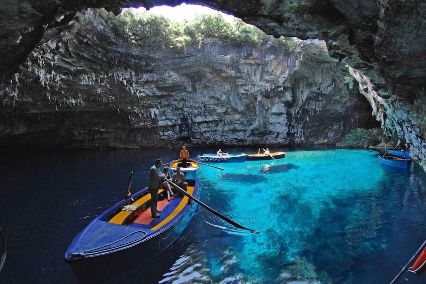 A group of people in canoes on a clear blue water body, surrounded by rocky cliffs and a cave entrance. 4