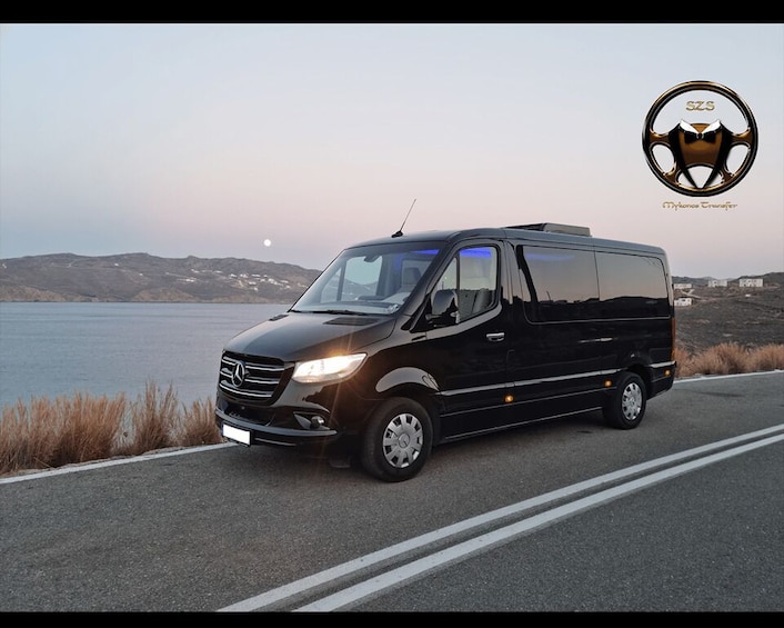 A black Mercedes-Benz Sprinter van parked on a road with a body of water and hills in the background. 3