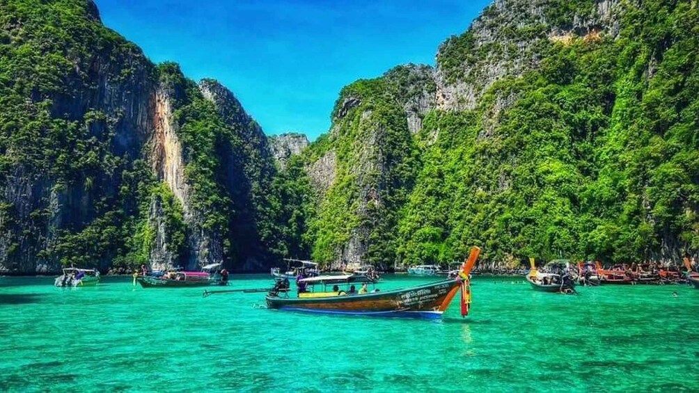A boat with passengers in turquoise waters surrounded by lush green cliffs. 3