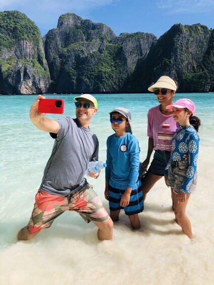 A family taking a selfie on a beach with clear turquoise water and limestone cliffs in the background. 5