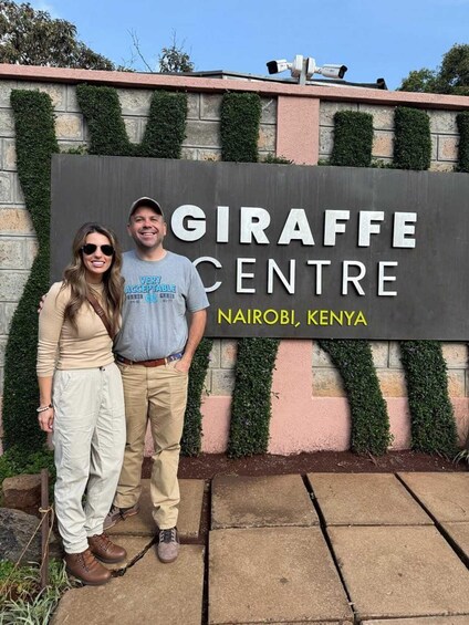 Two people standing in front of a sign that reads "GIRAFFE CENTRE" in Nairobi, Kenya. 1
