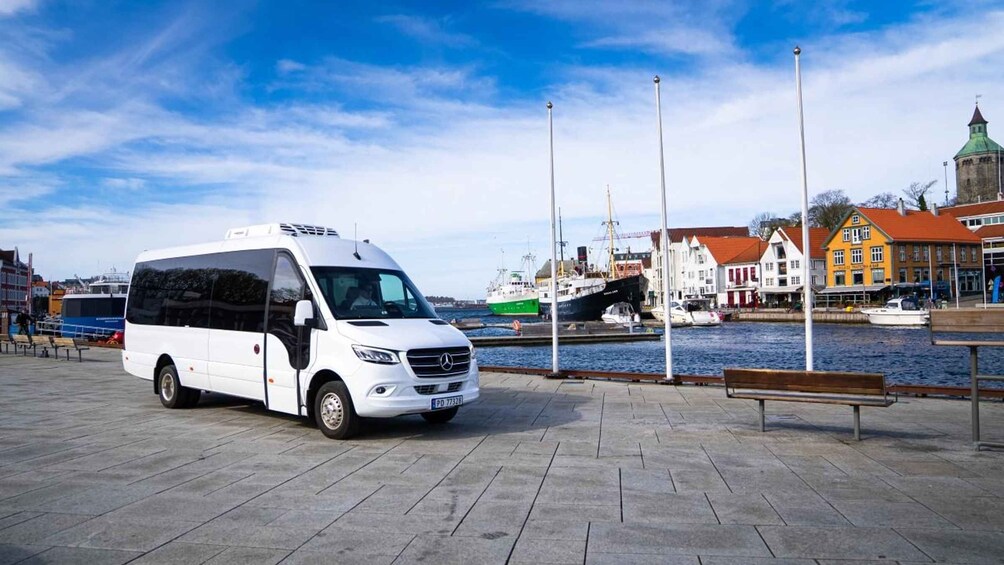 A white van parked on a waterfront promenade with boats docked in the background and colorful buildings along the shore. 2