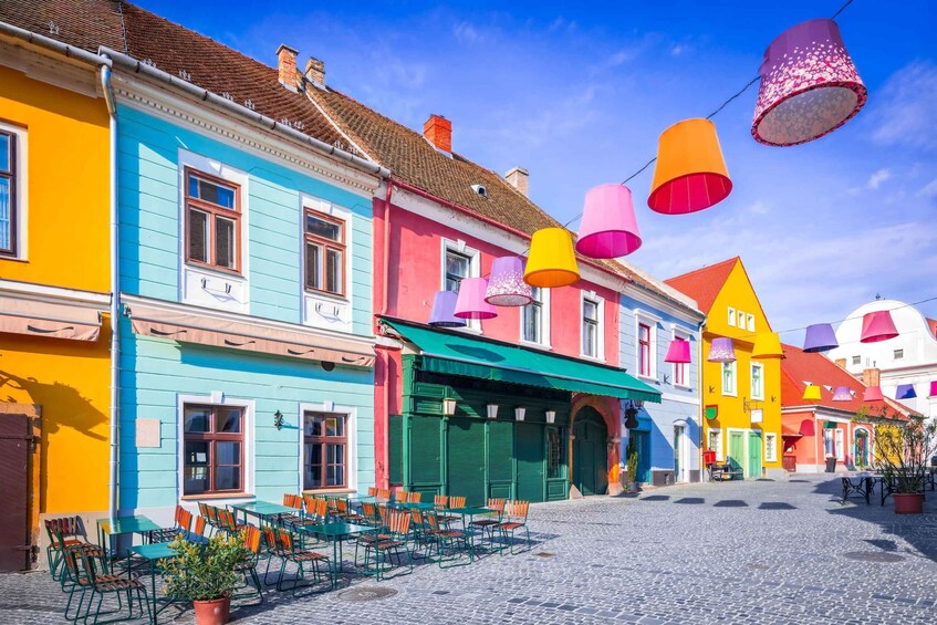 A cobblestone street lined with colorful buildings, outdoor seating, and hanging paper lanterns. 1