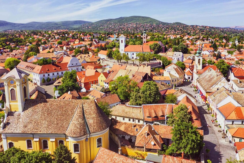 A historic town with red-roofed buildings, a prominent church, and a mountainous backdrop. 3