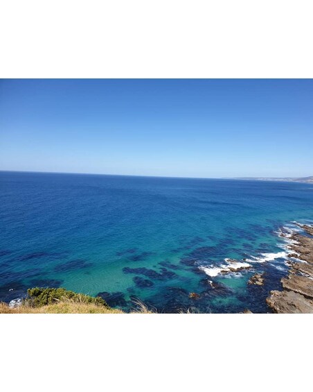 A coastal landscape with clear blue sea, rocky shoreline, and distant land. 3