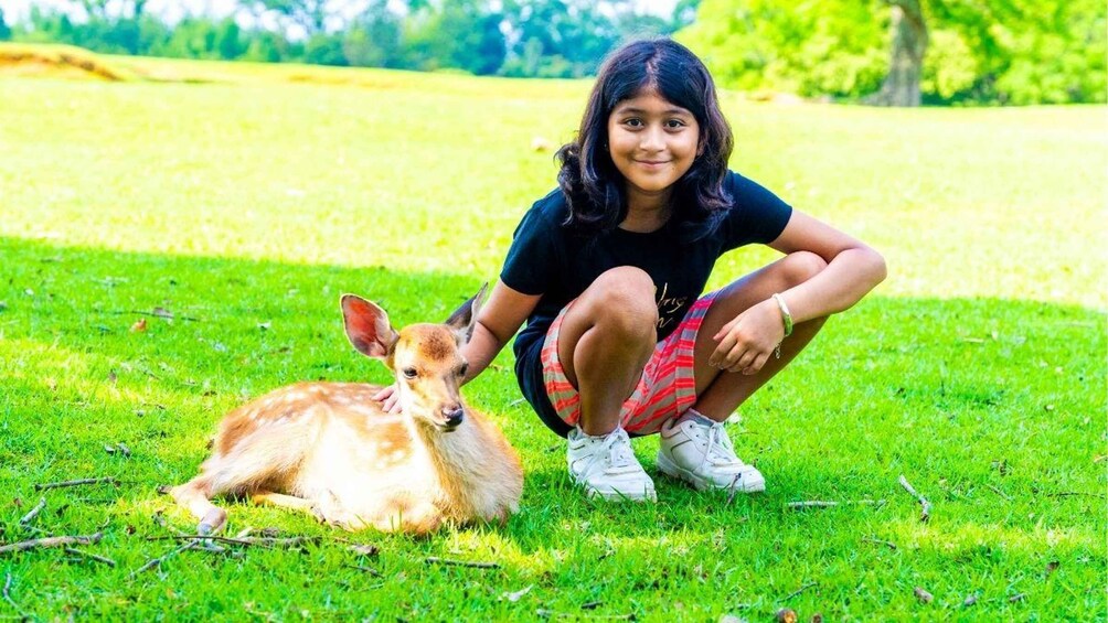 A person crouching on grass with a deer. 4