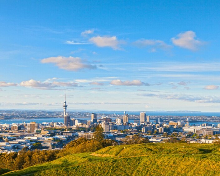 A cityscape with a prominent tower, green hills, and a clear blue sky. 5