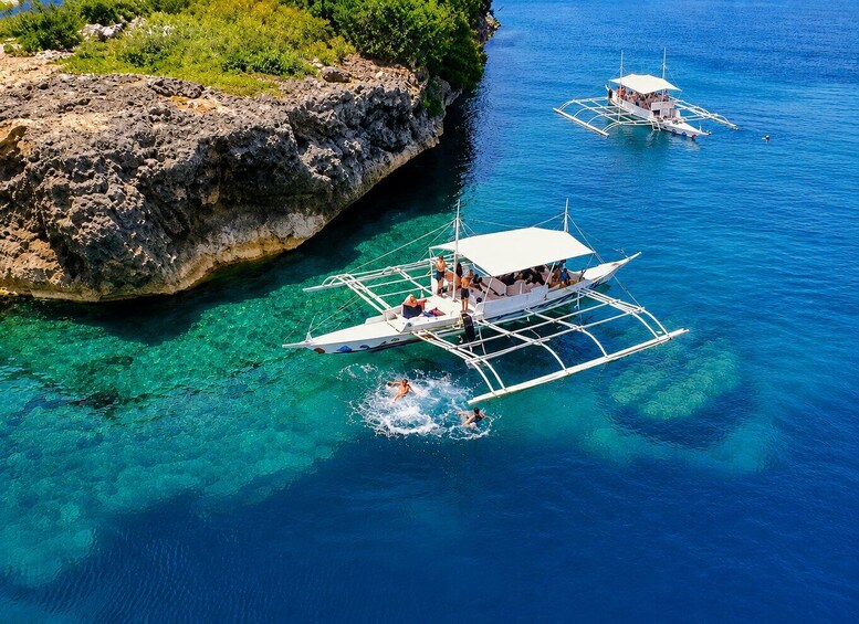 A clear blue sea with two traditional boats anchored near a rocky shore. 1