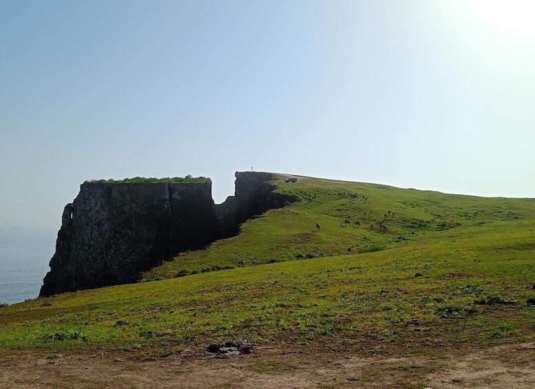 A grassy hill with a cliff edge and a vehicle parked on the top. 5