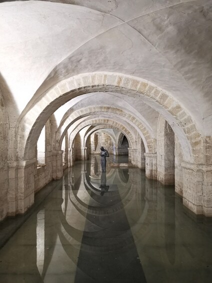 A stone corridor with arches and a reflective floor. 5