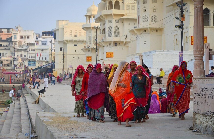 A group of women in traditional Indian attire walking along a street with historic buildings in the background. 1