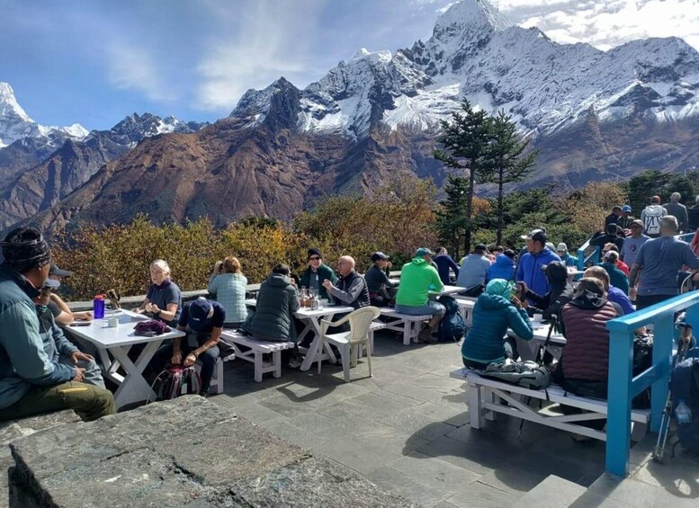 A group of people sitting at tables outdoors with a mountainous landscape in the background. 1