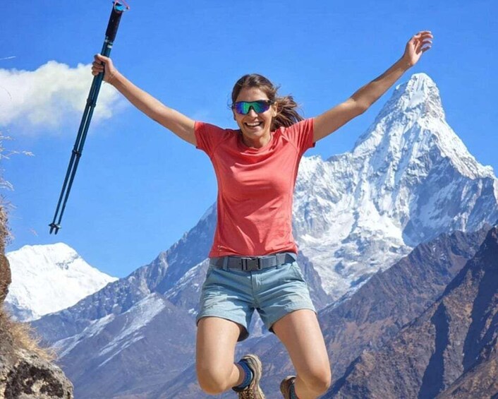 A person jumping with arms raised, holding a trekking pole, in front of a snow-capped mountain. 2