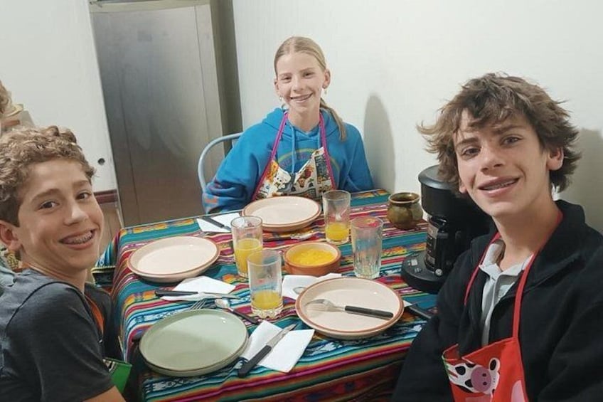Three people sitting at a table with plates, glasses, and a coffee maker. 3