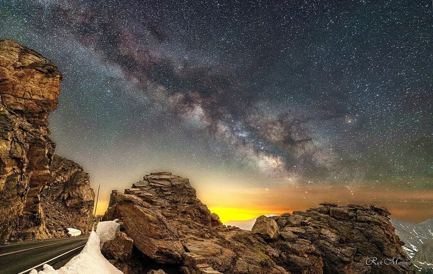 A starry night sky over rocky terrain with a road in the foreground. 1