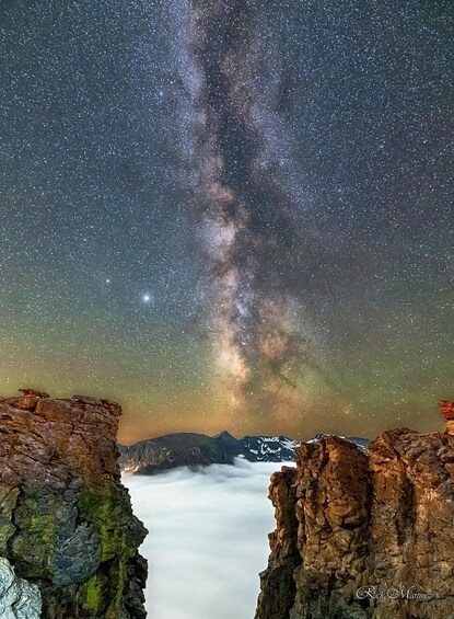 A starry night sky with the Milky Way visible, rocky cliffs, and a mountain range in the background. 2