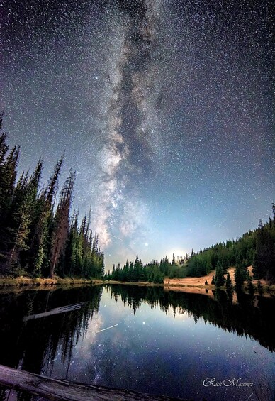 A starry night sky over a calm lake with a reflection of the Milky Way and trees. 3