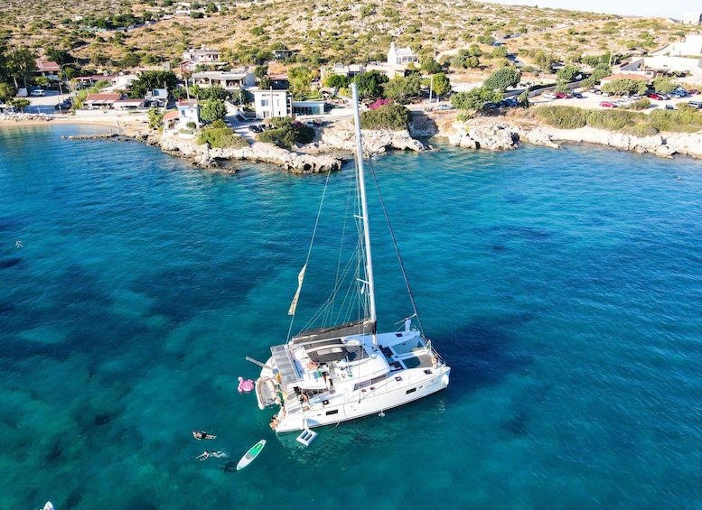 Un velero anclado cerca de un pueblo costero, con aguas azules cristalinas y terreno rocoso. 3