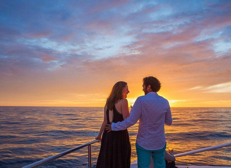 A couple standing on a boat deck during sunset with the ocean in the background. 1