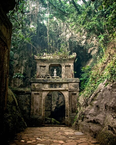 A stone archway with a statue, surrounded by dense forest and rocky terrain. 2