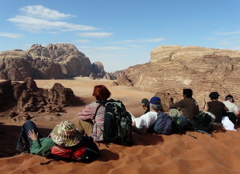 A group of people sitting on sand dunes with rocky formations in the background. 3