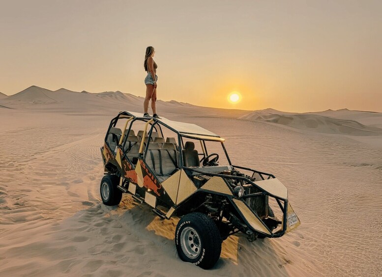 A person standing on a dune in a desert with a dune buggy. 1