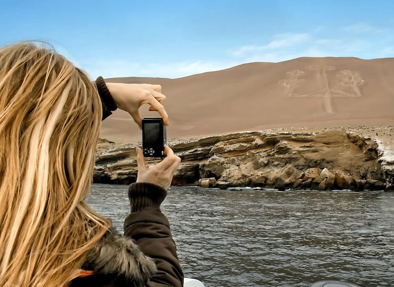 A person taking a photo of a desert landscape with sand dunes and rock formations. 5