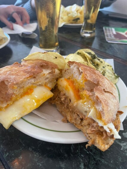 A sandwich cut in half, revealing melted cheese and shredded meat, on a plate with a side of chips. 3