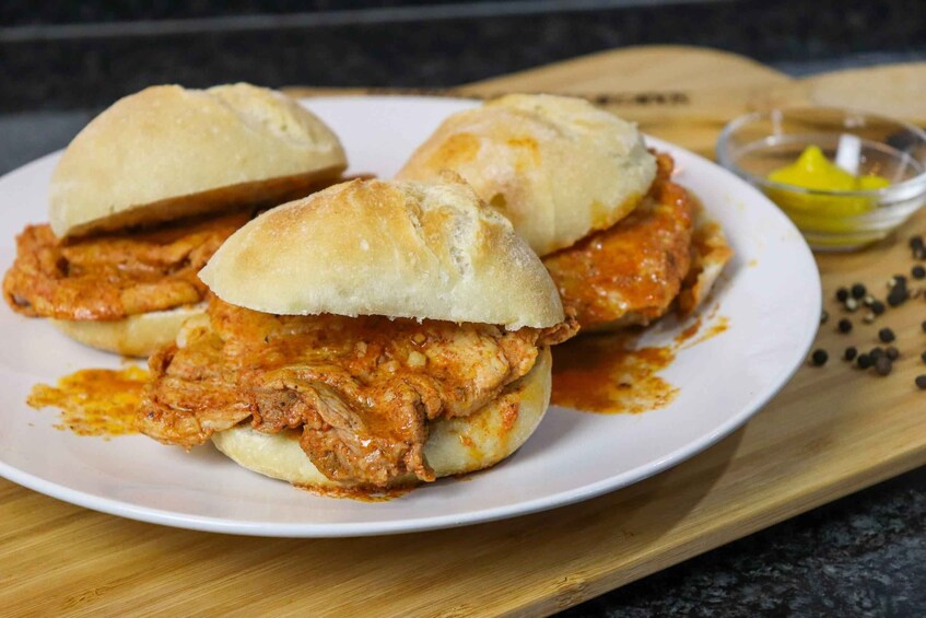 Two sandwiches with a red sauce, a small bowl of lemon wedges, and some black peppercorns on a wooden board. 1