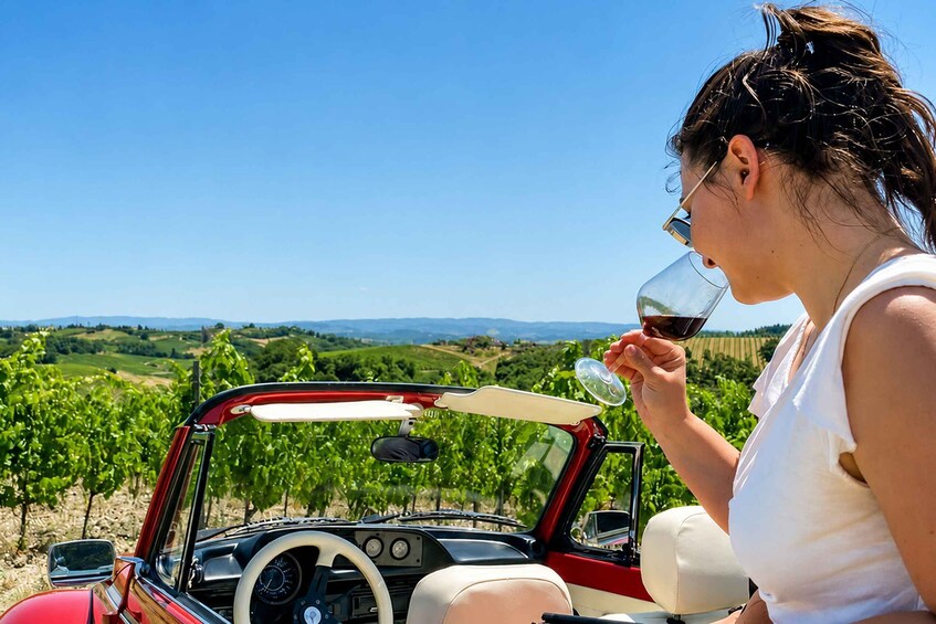 A person in a convertible car with a vineyard landscape in the background. 4