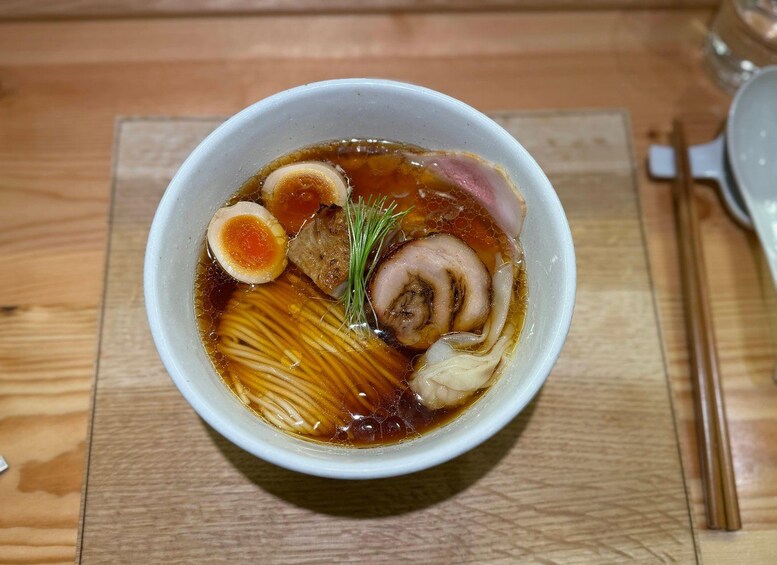A bowl of ramen with noodles, egg, pork, and seaweed on a wooden table. 2