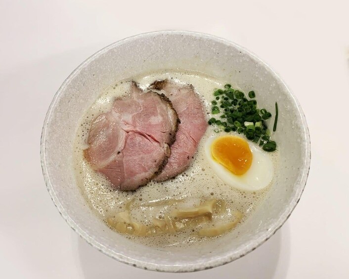 A bowl of ramen with sliced meat, a soft-boiled egg, green onions, and noodles. 4