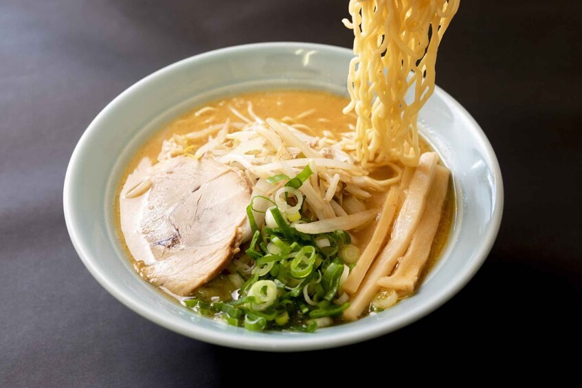 A bowl of ramen with noodles, sliced pork, green onions, and a clear broth. 1