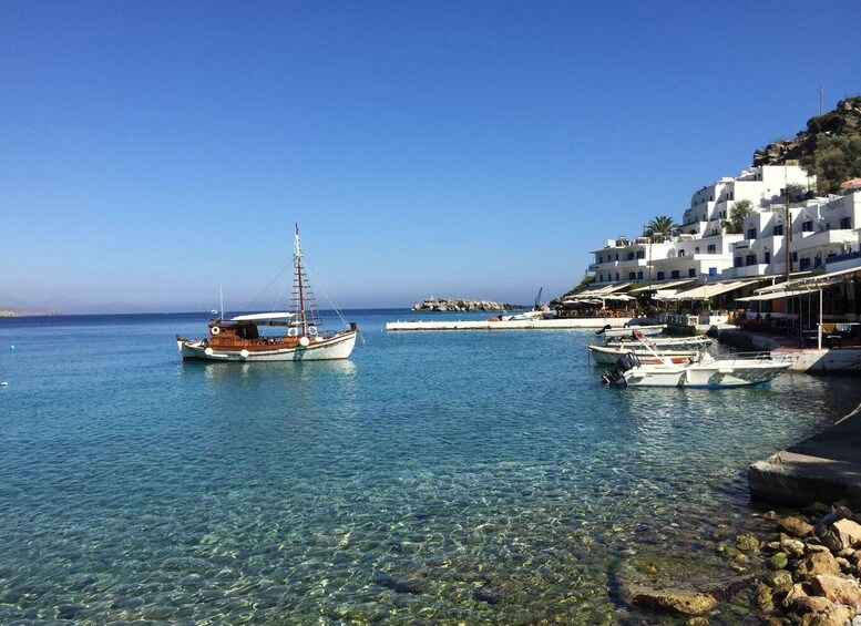 A coastal scene with a clear blue sea, a wooden boat, and white buildings with blue accents on a hillside. 2