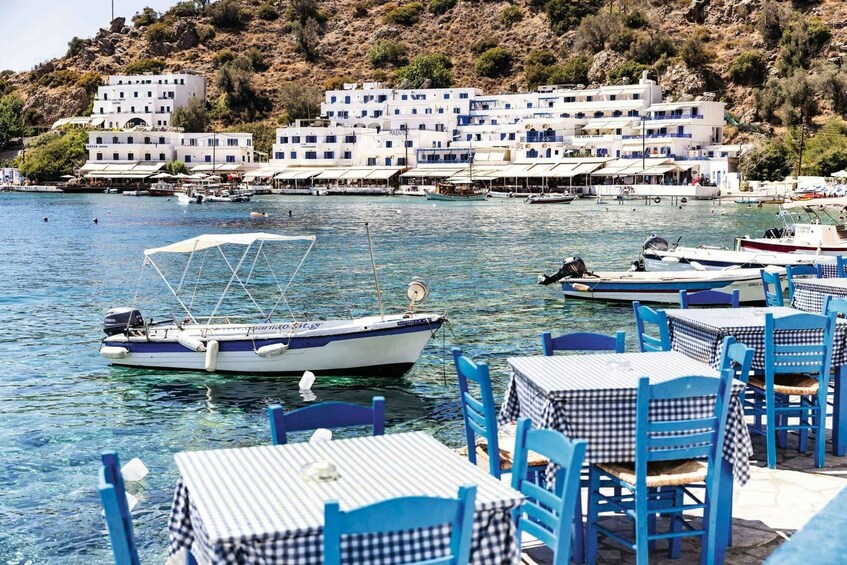 A coastal town with white buildings, clear blue waters, and boats anchored near tables and chairs. 3